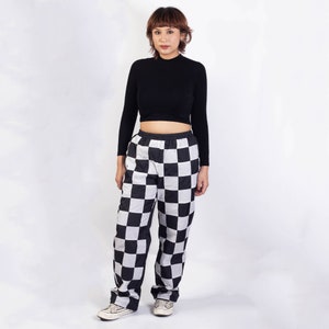 May include: A person wearing a black mock neck top and black and white checked trousers.