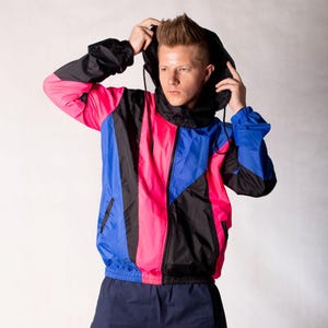 May include: A black, pink, and blue color block windbreaker jacket with a zipper closure and a hood.