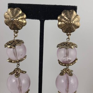 May include: A pair of dangle earrings with two pink glass beads and gold-toned metal accents.