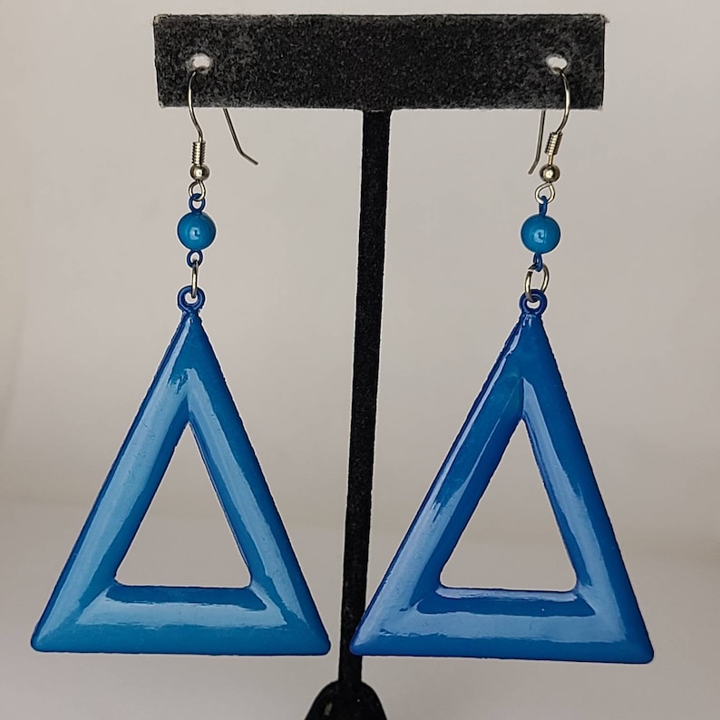 May include: A pair of blue triangle earrings with a silver hook and a blue bead on the top of each earring.