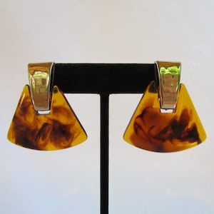 May include: A pair of brown and gold tone earrings with a triangular shape. The earrings have a silver tone metal band around the top.