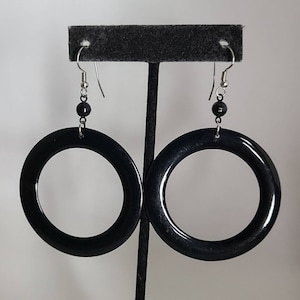 May include: A pair of black hoop earrings with silver hooks and black beads. The earrings are hanging from a black stand.