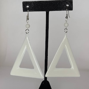 May include: A pair of white triangle earrings with a smaller triangle cutout in the center. The earrings are hanging from silver hooks.