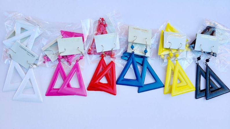 May include: Assortment of triangle-shaped earrings in various colors, including white, pink, red, blue, yellow, and black. The earrings are packaged in clear plastic bags with a small card that says "Fashion Earrings".