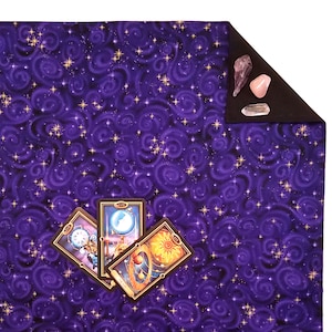 May include: Purple tarot cloth with a swirling star pattern and three tarot cards featuring celestial imagery. The cards are the World, the Sun, and the Moon.