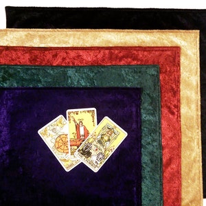 May include: Five velvet tarot cloths in different colors: black, beige, red, green, and purple. The cloths are stacked on top of each other, with the purple cloth on the bottom. Four tarot cards are placed on top of the purple cloth, showing the Wheel of Fortune, The Chariot, and two other cards.