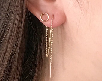 May include: A gold hoop earring with a dangling chain and a small gold bar at the end. The earring is worn in the left ear.