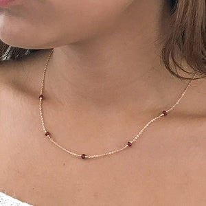 May include: A delicate gold chain necklace with small, evenly spaced, dark red beads.