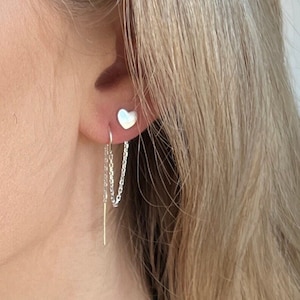 May include: A silver heart-shaped earring with a delicate chain dangling from the bottom. The chain is attached to a small silver bar.