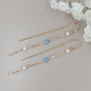 May include: Three pairs of gold dangle earrings with a pearl and a blue crystal charm on each earring.