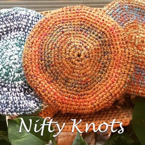 May include: Three crocheted round coasters in different colors. The coasters are made with a variety of colorful yarns and have a circular pattern. The coasters are sitting on a woven wicker surface. The text "Nifty Knots" is visible in the bottom of the image.