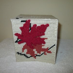 May include: A white tissue box cover with a red and orange leaf design. The leaves are embroidered on the front of the box.