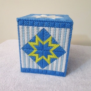 Può includere: Un copri scatola di fazzoletti blu e bianco con un motivo a stella gialla. Il copri scatola è realizzato in tela di plastica ed è cucito a mano.