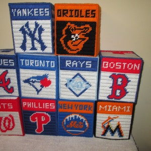 May include: A set of 10 tissue box covers featuring different Major League Baseball team logos. The logos are embroidered on the covers, which are made of a white canvas-like material. The logos include the New York Yankees, Baltimore Orioles, Atlanta Braves, Toronto Blue Jays, Tampa Bay Rays, Boston Red Sox, Washington Nationals, Philadelphia Phillies, New York Mets, and Miami Marlins.