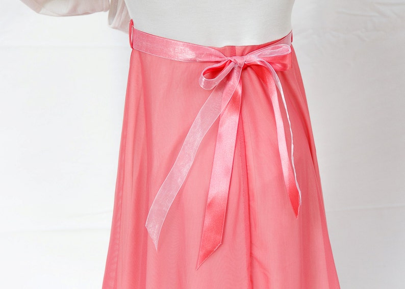 May include: A coral pink tulle skirt with a satin ribbon tied in a bow at the back.