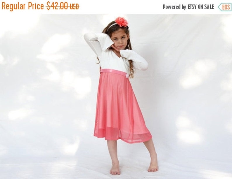 May include: A young girl wearing a white long-sleeved top with a pink tulle skirt and a pink flower headband.