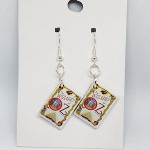 May include: Silver dangle earrings with a book charm featuring the cover of "The Wizard of Oz".