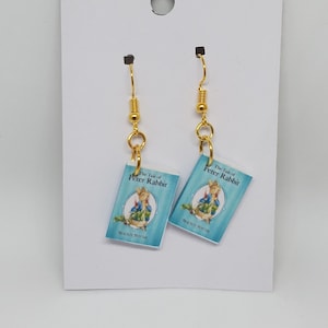 May include: A pair of gold dangle earrings with miniature blue book charms that say "The Tale of Peter Rabbit" on the front.