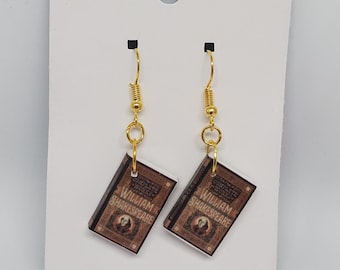 May include: A pair of gold dangle earrings with a book charm. The book charm is brown with gold accents and features the text "William Shakespeare".