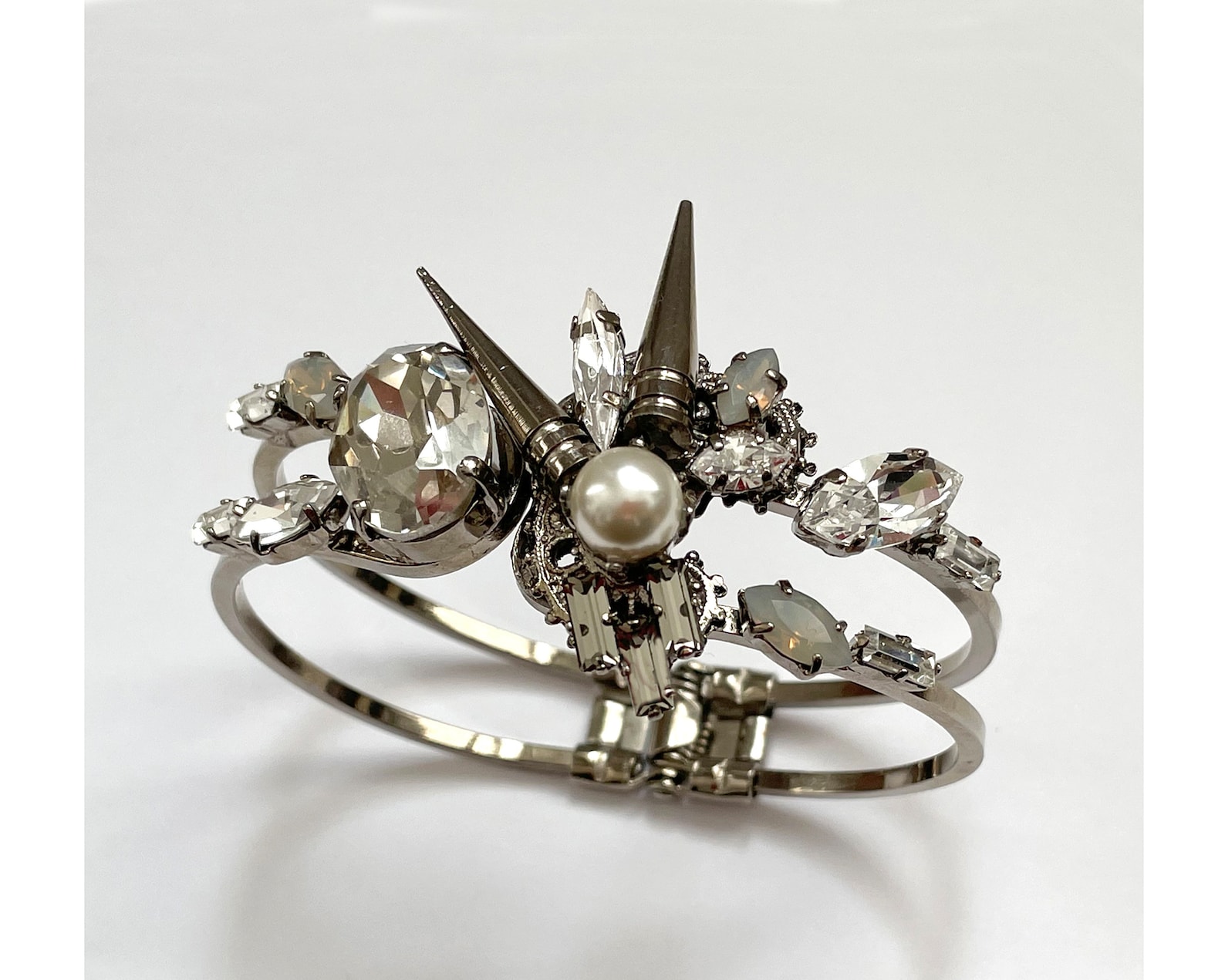 Swarovski crystal and pearl cuff goth bracelet with silver spikes and opal accents on white background