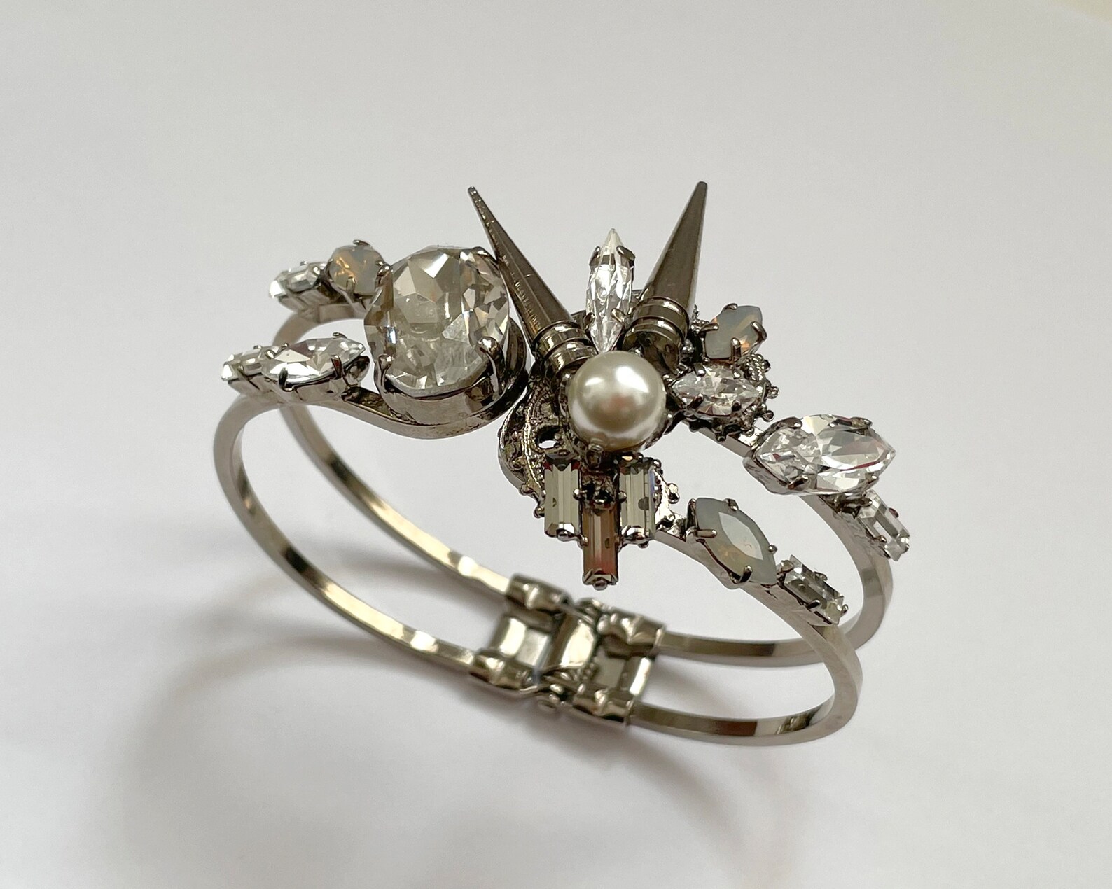 Angled side view of silver cuff bracelet with pearl, crystals, and gothic detailing