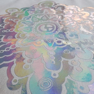 May include: A white canvas tote bag with a large iridescent mandala design. The mandala is a circular pattern with intricate details and a rainbow of colors.