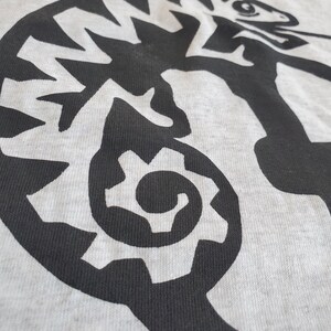 K&ouml;nnte beinhalten: Ein graues T-Shirt mit einem schwarzen und wei&szlig;en Grafikdruck eines Cham&auml;leons. Das Cham&auml;leon ist mit seinem Schwanz im Maul eingerollt.