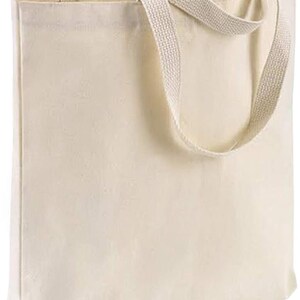 May include: A plain white canvas tote bag with two long, cream-colored straps.