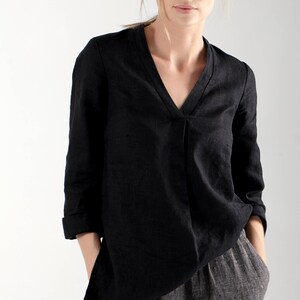 Puede incluir: Una blusa de lino negra con cuello en V y mangas largas, combinada con pantalones de lino grises.