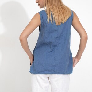 May include: A sleeveless, light blue linen top with a relaxed fit. The top is worn with white linen pants.