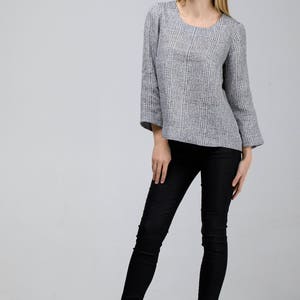 May include: A woman wearing a gray and white striped top with 3/4 sleeves and black skinny jeans. She is wearing black ankle boots with laces.