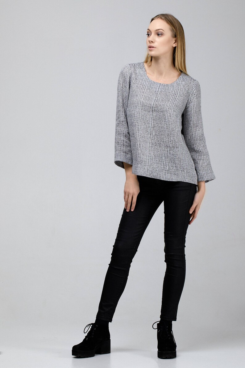 May include: A woman wearing a gray and white striped top with 3/4 sleeves and black skinny jeans. She is wearing black ankle boots with laces.