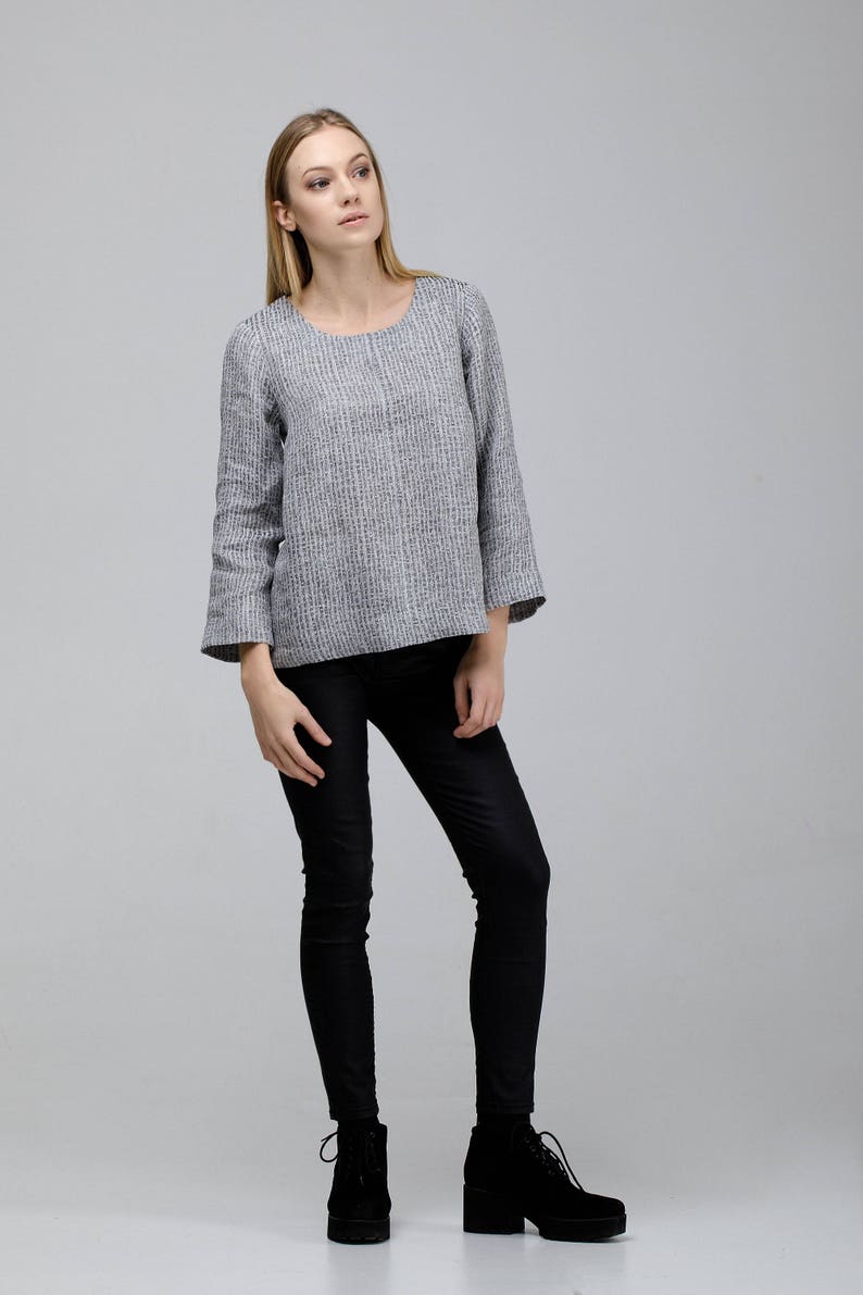 May include: A woman wearing a gray and white striped long-sleeved shirt with black pants and black ankle boots.