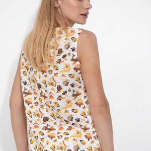 May include: A sleeveless white linen top with a floral print in shades of yellow, orange, and brown. The print features small flowers and leaves.