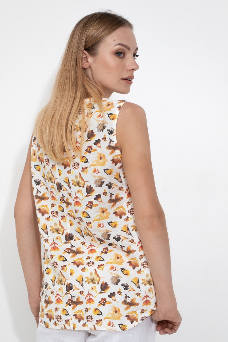 May include: A sleeveless white linen top with a floral print in shades of yellow, orange, and brown. The print features small flowers and leaves.