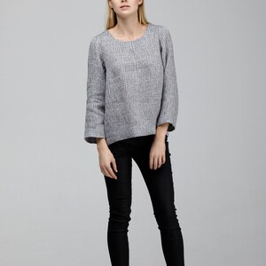 May include: A woman wearing a gray and white striped long-sleeved shirt with black skinny jeans and black ankle boots.