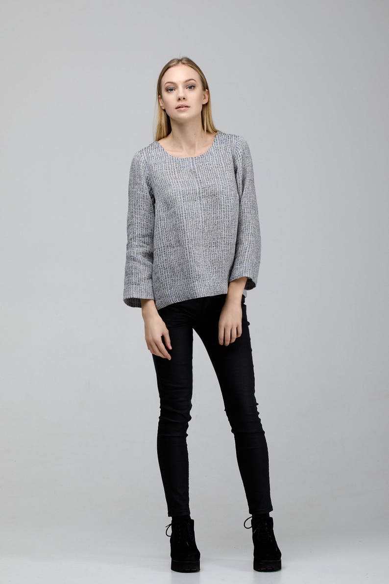 May include: A woman wearing a gray and white striped long-sleeved shirt with black skinny jeans and black ankle boots.