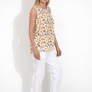 May include: A white sleeveless top with a floral print in shades of yellow, orange, and brown. The top is paired with white linen pants and beige sandals.