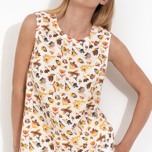 May include: A sleeveless white linen top with a floral print featuring yellow, orange, and brown leaves and flowers.