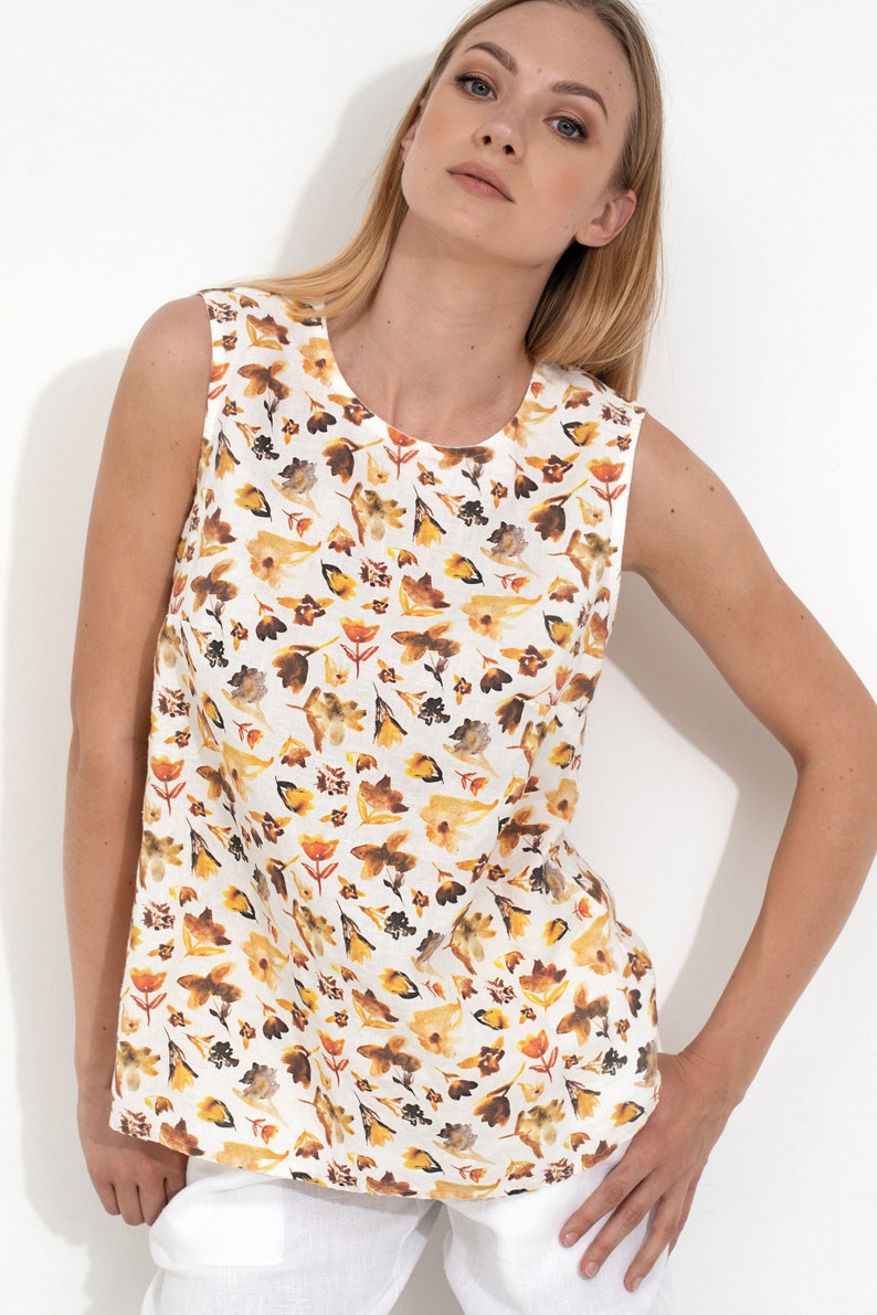 May include: A sleeveless white linen top with a floral print featuring yellow, orange, and brown leaves and flowers.