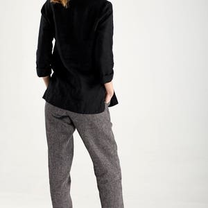 Puede incluir: Una mujer con una camisa de lino negra y pantalones de lino grises. Est&aacute; de pie de espaldas a la c&aacute;mara con las manos en los bolsillos.