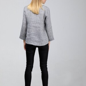 May include: A woman wearing a gray and white striped linen jacket with black skinny jeans and black ankle boots.