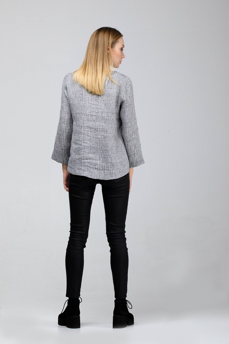 May include: A woman wearing a gray and white striped linen jacket with black skinny jeans and black ankle boots.