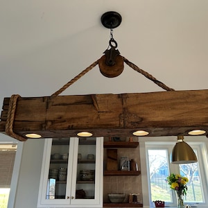 May include: A rustic wooden chandelier with a rope and pulley design. The chandelier has four light bulbs and is hanging from the ceiling.