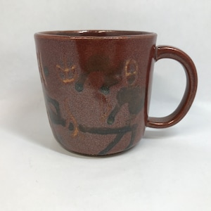 May include: A brown ceramic mug with a handle. The mug has a dark brown glaze with a pattern of gold and black lines and shapes.