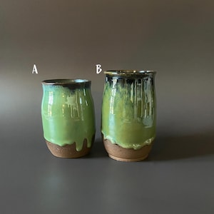 May include: Two handmade ceramic tumblers. The tumblers are glazed in a vibrant green color that drips down the sides, with a dark brown rim and base. The tumblers are labeled A and B.