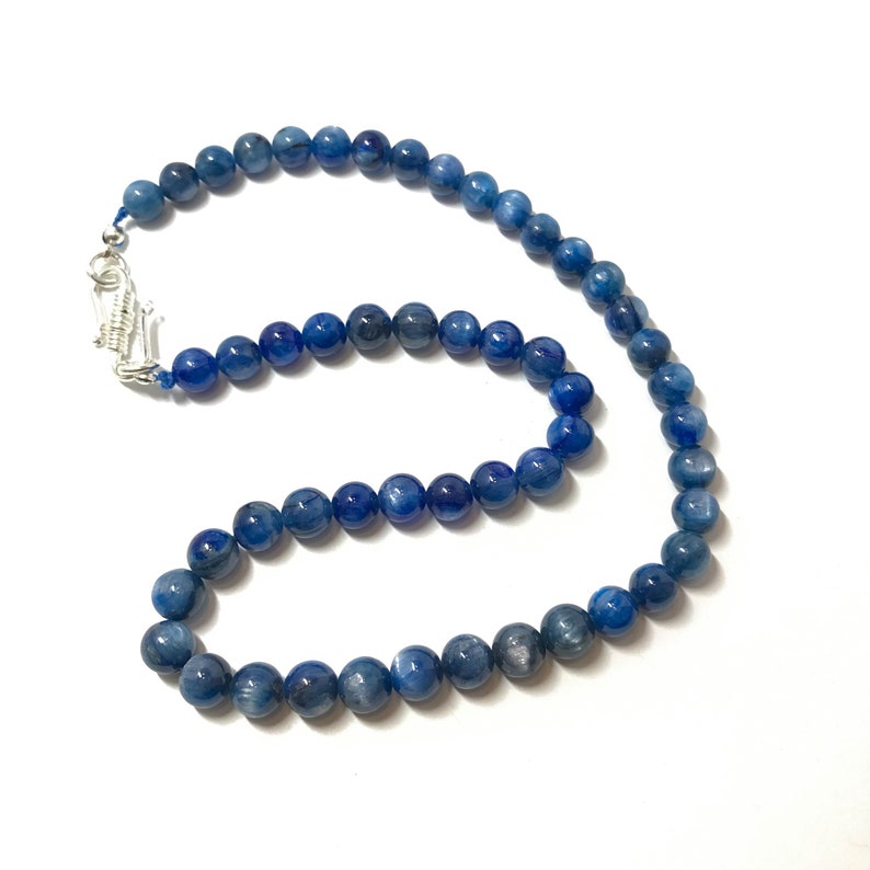 May include: A blue gemstone necklace with silver clasp. The necklace is made of round beads and is approximately 18 inches long.