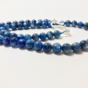 May include: A blue gemstone necklace with silver clasps. The necklace is made of round beads with a marbled pattern.