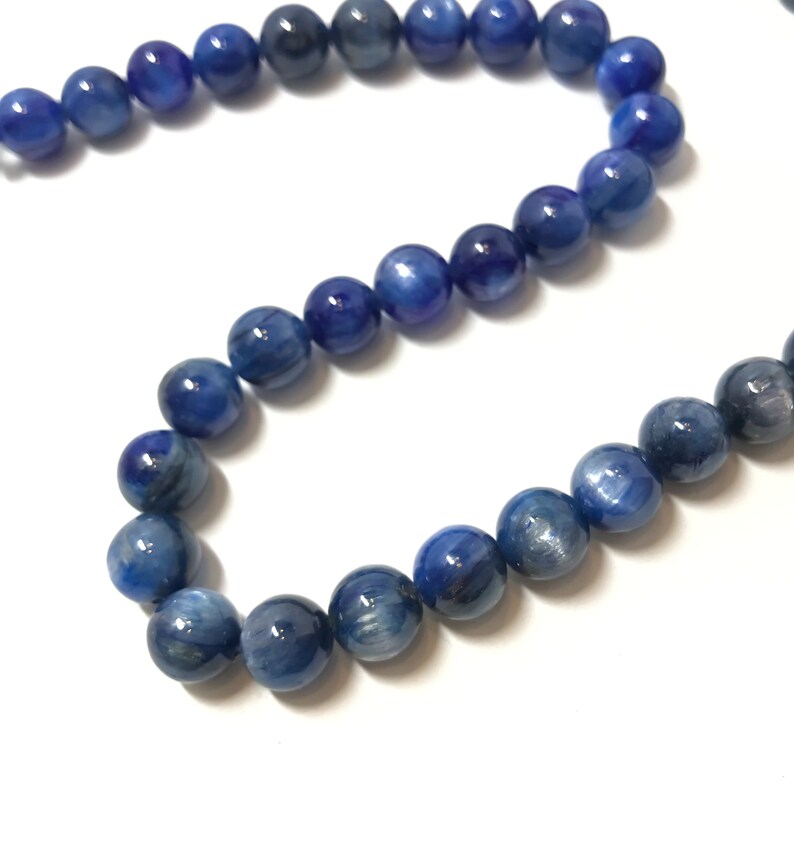 May include: A strand of blue gemstone beads. The beads are round and have a smooth, polished finish. The beads are strung on a clear thread.