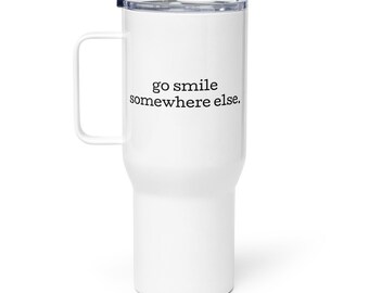 May include: White travel mug with a handle and a black lid. The mug has the phrase "go smile somewhere else" printed in black. The mug is designed to keep beverages hot or cold.